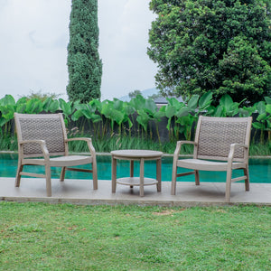 Two wicker chairs and a small table on a patio by a pool with greenery in the background.