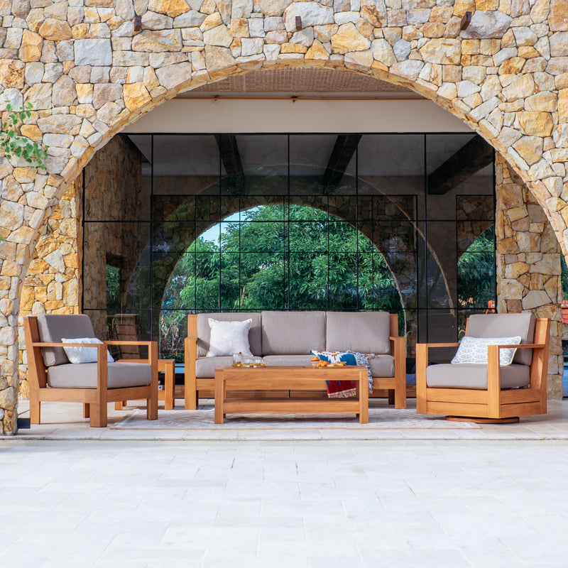 Outdoor patio set with wooden chairs and sofa against a stone wall.