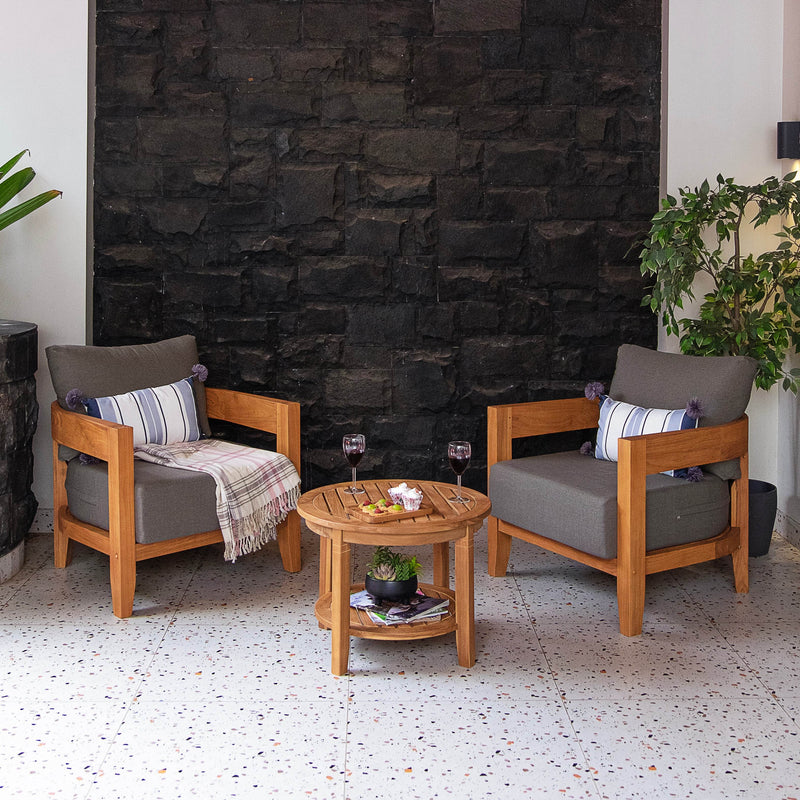 Two wooden chairs with gray cushions and a small round table against a stone wall.